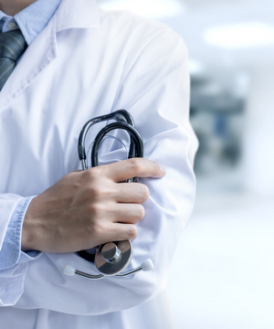 Grafika przedstawia postać lekarza z białym kitlu trzymającego w dłoni stetoskop
